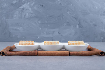 Small cookies on a serving platter framed with cinnamon sticks on marble background