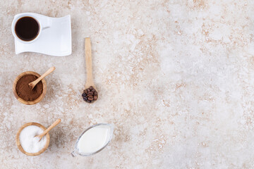 A cup of coffee, milk, sugar, coffee powder and coffee beans on marble background