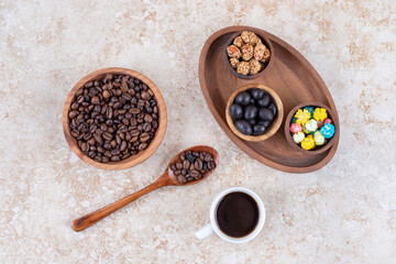 Snack assortment in a wooden tray next to coffee beans and a cup of brewed coffee on marble background