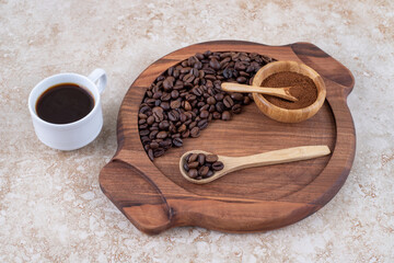 A cup of coffee next to a tray of coffee beans and ground coffee powder on marble background