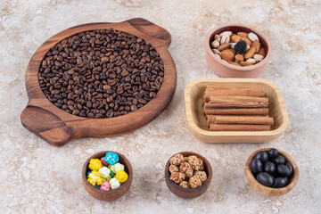 Portions of candies, assorted nuts, glazed peanuts, cinnamon sticks and coffee beans on marble background