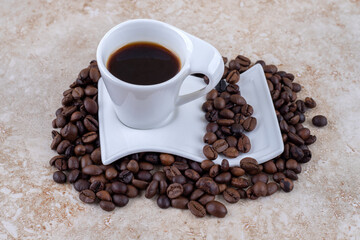 A cup of coffee on a saucer sitting on a pile of coffee beans on marble background