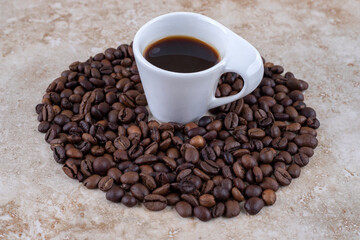 Neatly arranged coffee bean pile surrounding a cup of coffee on marble background