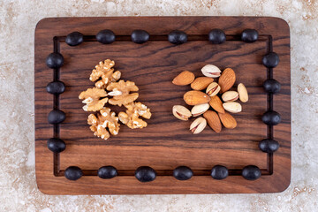 An arrangement of chocolate candies and nut piles on a board on marble background