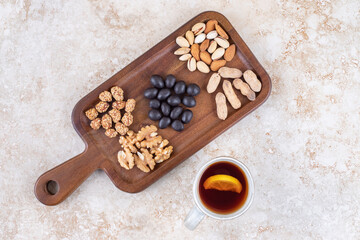 Mug of tea next to a snack serving with small piles of nuts and candy on a board on marble background