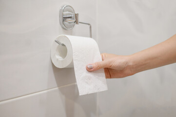 A woman takes out toilet paper from a roll of toilet paper.Close-up.The concept of problems with the intestines,cystitis