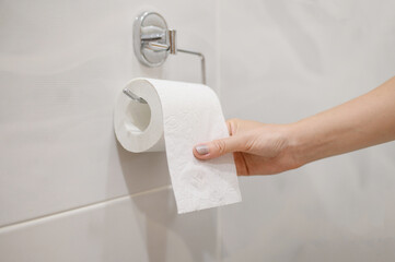 A woman takes out toilet paper from a roll of toilet paper.Close-up.The concept of problems with...