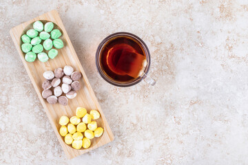 A cup of tea and assorted candies bundled in a small wooden tray on marble background