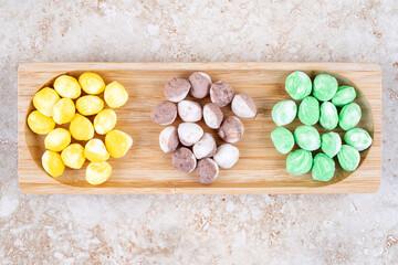 Assorted candies bundled in a small wooden tray on marble background