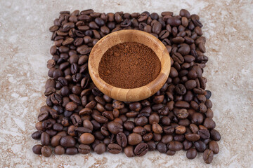 Small bowl with coffee powder surrounded with a small pile of coffee beans on marble background