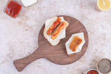 Lunch arrangement with fish fingers on bread and various seasonings and condiments on marble background