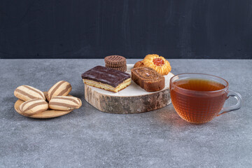 Assortment of cakes and cookies and a cup of tea on marble background