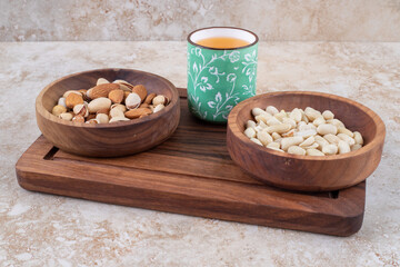 Bowls of nuts and a cup of juice on a board on marble background