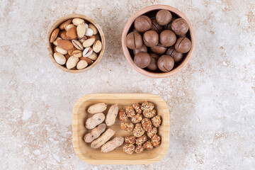 Obraz na płótnie Canvas Assorted nuts in bowls next to a bowl of chocolate balls on marble background