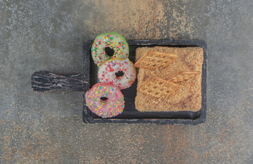 Cracker-topped cake slice and small donuts on a black tray on wooden background