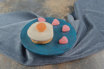Heart shaped marmelades and white chocolate topped cake on a board on wooden background