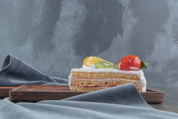 Fruit and cream topped cake slice on a small wooden board on wooden background
