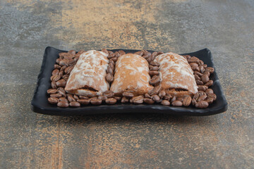 Coffee beans and cookies on a black platter on wooden background