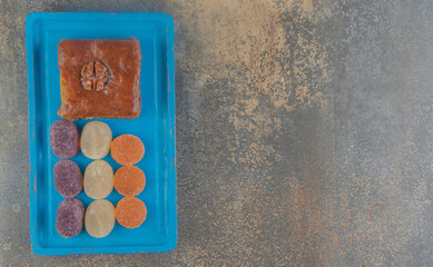Marmelades next to a piece of bakhlava on a blue platter on wooden background
