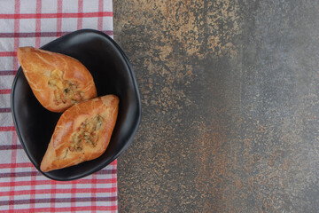 A small serving of pide buns in a black bowl on a towel on wooden background