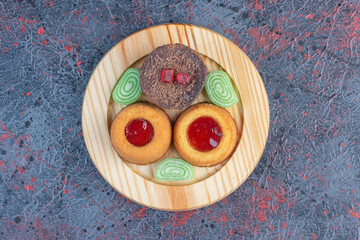 Various cakes and marmalades on a wooden platter on abstract background