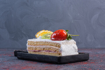 Fruit topped cake slice on a black board on abstract background