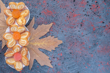 Flaky cookies and marmalades in a serving plate on plane tree leaves on abstract background