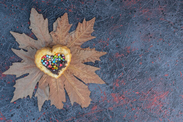 Heart cake with chocolate and candy filling on plane tree leaves on abstract background