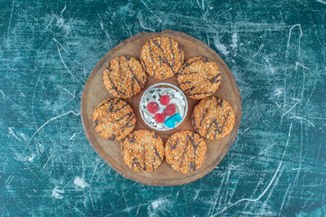 Cookies encircling a cupcake on a wooden board on blue background