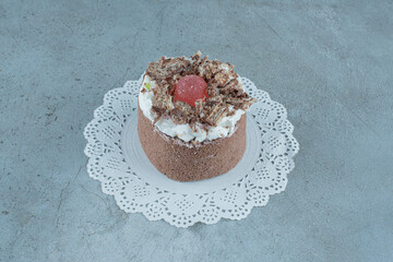 Cream and marmelade topped cake on a doily on marble background