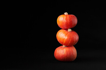 Three small bright orange pumpkins stacked on top of each other against the black background. Decoration for the Halloween holiday.