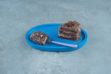 Small pieces of chocolate cake and a fork on a blue platter on marble background