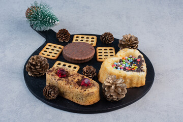 Pine cones, cookies, cakes and crackers on a black board on marble background