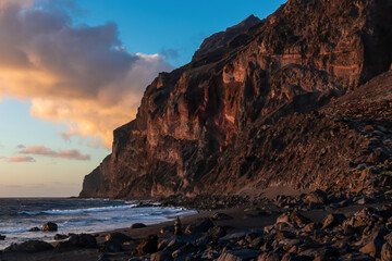 Fototapeta na wymiar Scenic view during sunset on the volcanic sand beach Playa del Ingles in Valle Gran Rey, La Gomera, Canary Islands, Spain, Europe. Massive cliffs of the La Mercia range. Calm atmosphere at the seaside