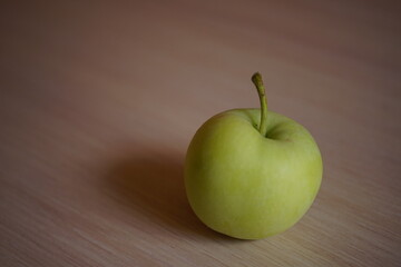 One ripe green apple on pale wooden table.