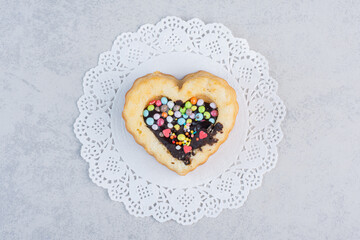 Small cake with chocolate and candy filling on a doily on marble background - obrazy, fototapety, plakaty