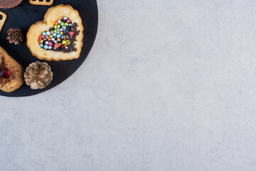 Pine cones, cookies, cakes and crackers on a black board on marble background