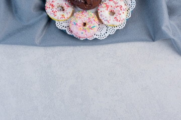 Donuts around a chocolate cupcake on a doily on marble background