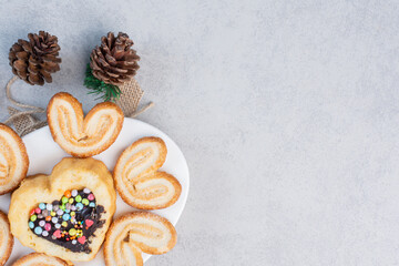 Flaky cookies and a small cake on a platter next to pine cones on marble background