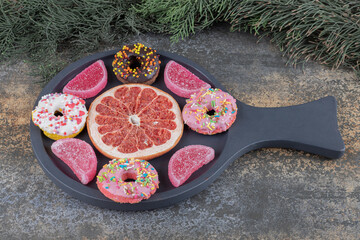 Small donuts, marmelades and a grapefruit slice next to a pine branch on wooden background