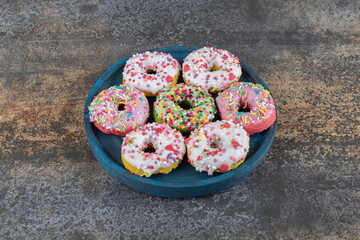 Worn-out platter with candy sprinkled donuts on wooden background