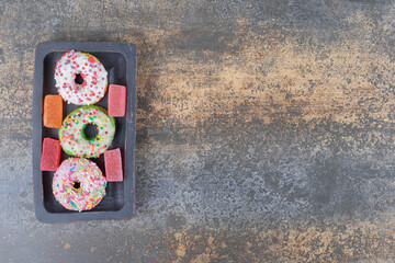 Black wooden platter with bite-sized donuts and marmelades on wooden background