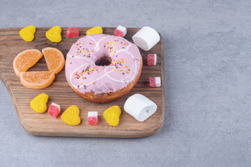 Marshmallows, marmelades and a donut on a wooden board on marble background