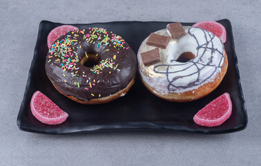 Black platter with donuts and marmelades on marble background