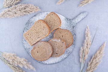Flour covered board with bread slices next to feather grass stalks on marble background