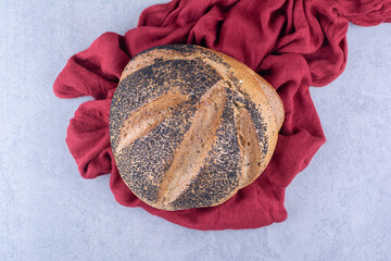 Piece of cloth under a loaf of black sesame coated bread on marble background
