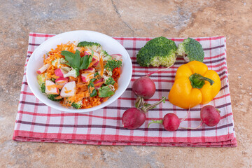 Mixed salad platter next of various vegetables on a towel on marble background