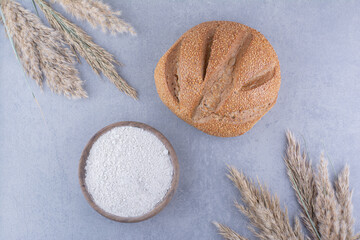 Bowl of flour, loaf of bread and stalks of dried feather grass on marble background