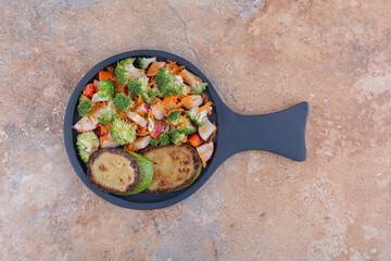 Small pan with fried zucchini slices and a mixed vegetable salad on marble background