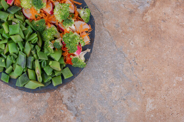 Tray of mixed vegetable salad and chopped bean pulses on marble background
